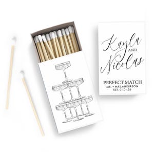 a matchbox with a stack of champagne glasses and a note that reads "Perfect Match Mr. + Mrs. Anderson EST 01.01.26".