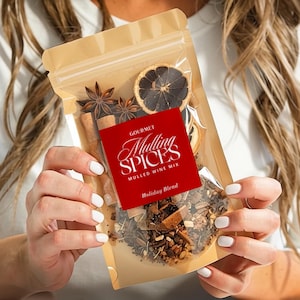 May include: A clear, resealable bag filled with mulling spices, including star anise, cinnamon sticks, and dried citrus. A red label reads "Gourmet Mulling Spices, Mulled Wine Mix, Holiday Blend". The bag is held in front of a white shirt.