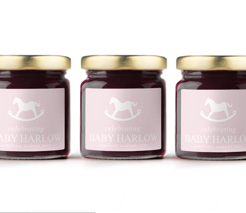 May include: Three glass jars with gold lids filled with a dark red preserve. Each jar has a pink label with a white rocking horse graphic and the text "celebrating BABY HARLOW ARRIVING AUGUST 2023".