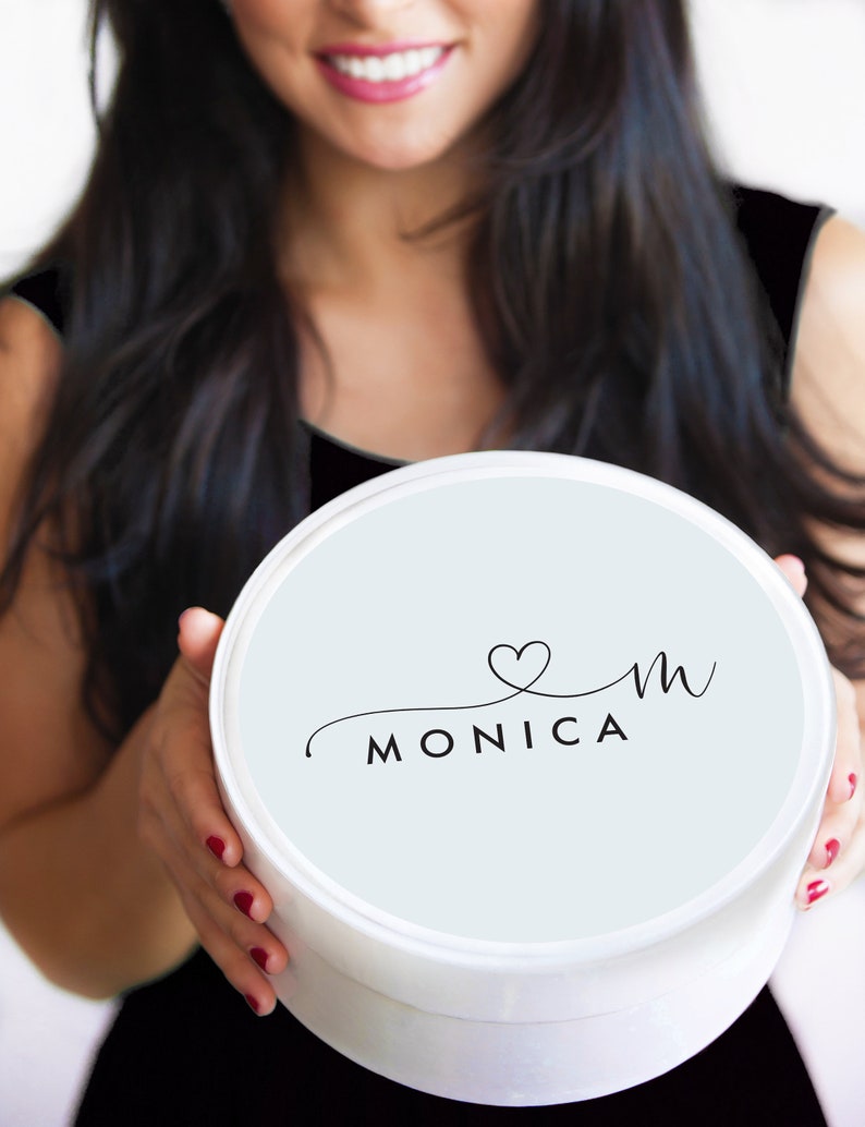 Puede incluir: Una caja redonda blanca con una tapa azul claro. La tapa tiene un logotipo negro en cursiva que dice "&hearts;m MONICA".