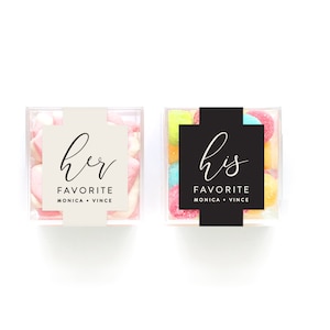 May include: Two clear square containers filled with colorful candies. One container has a white label with the text "her favorite Monica + Vince" and the other container has a black label with the text "his favorite Monica + Vince".