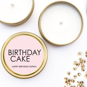 以下が含まれることがあります： ピンクのラベルが付いたゴールドのキャンドル缶。ラベルには「Birthday Cake」と「Happy Birthday Sophia」と書かれています。