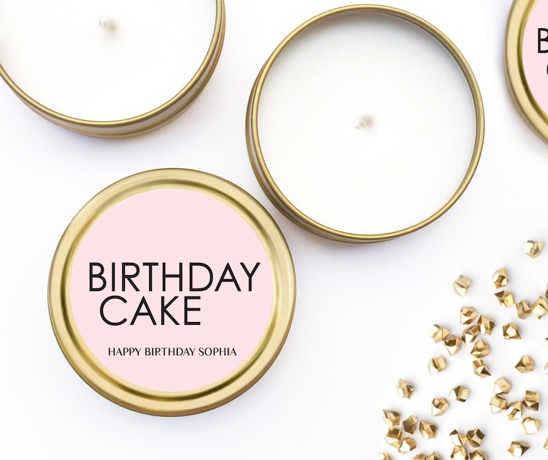 以下が含まれることがあります： ピンクのラベルが付いたゴールドのキャンドル缶。ラベルには「Birthday Cake」と「Happy Birthday Sophia」と書かれています。