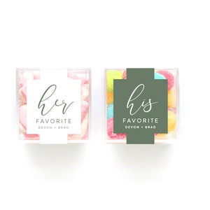 May include: Two clear plastic containers filled with colorful candies. One container has a white label that says "her favorite Devon + Brad". The other container has a green label that says "his favorite Devon + Brad".