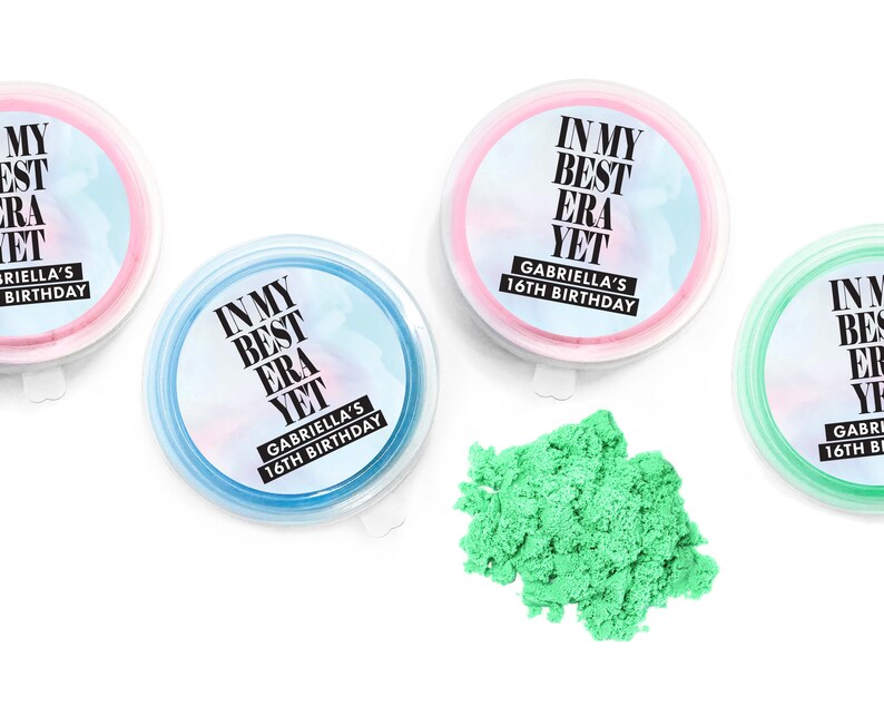 May include: Three clear plastic containers with lids, each filled with a different color of sand. The containers have labels that say "In My Best Era Yet" and "Gabriella's 16th Birthday".