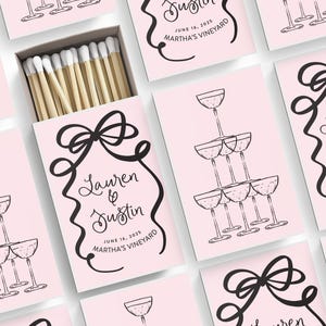 May include: Pink matchboxes with black and white illustrations of champagne glasses and a bow. The text on the boxes reads "Lauren & Justin" and "June 16, 2025 Martha's Vineyard".