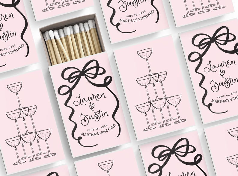 May include: Pink matchboxes with black and white illustrations of champagne glasses and a bow. The text on the boxes reads "Lauren & Justin" and "June 16, 2025 Martha's Vineyard".