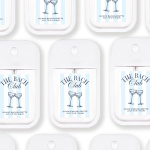 multiple white spray bottles with blue and white labels, each featuring a design of two champagne glasses and the text "The BACH Club" and "Quinn's Bachelorette July 15-18 Miami".