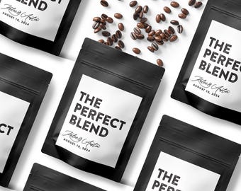 May include: Multiple black coffee pouches with white labels featuring the text THE PERFECT BLEND, the names Kalee & Austin, and the date AUGUST 10, 2024. Scattered roasted coffee beans are positioned between the pouches on a white surface.