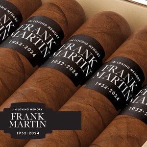 May include: A close-up of a box of cigars with black labels that read "In Loving Memory Frank Martin 1952-2024".