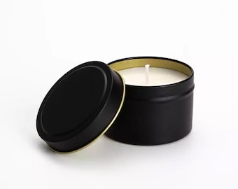 May include: A black candle tin with a gold rim and a white candle inside. The lid is off and sitting next to the tin.