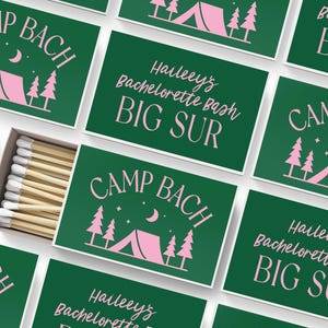 May include: A collection of rectangular matchboxes with a dark green background and pink graphics. The designs feature a tent, pine trees, a crescent moon, and stars with the text CAMP BACH or Haileey's Bachelorette Bash BIG SUR. One box is open.