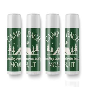 May include: Four green and white lip balm tubes with the text "CAMP BACH" and "MOAB, UT" printed on them. The tubes have a camping theme with a tent and pine trees.