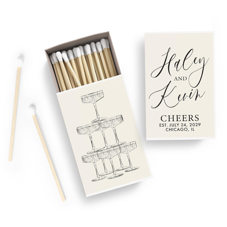 a matchbox with a design of champagne glasses, and a card with the names 'Haley and Kevin' and the date 'CHEERS EST. JULY 24, 2019 CHICAGO, IL'.