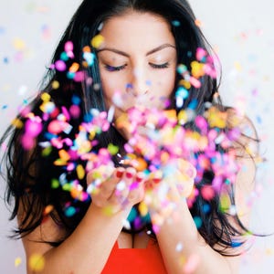 Pu&ograve; includere: Una donna con lunghi capelli neri soffia coriandoli dalle sue mani. I coriandoli sono multicolori e creano un'atmosfera festosa.