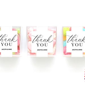 May include: Three clear plastic boxes filled with colorful candies. Each box has a white label with black text that reads "thank you" and "Jaclyn & Mike".