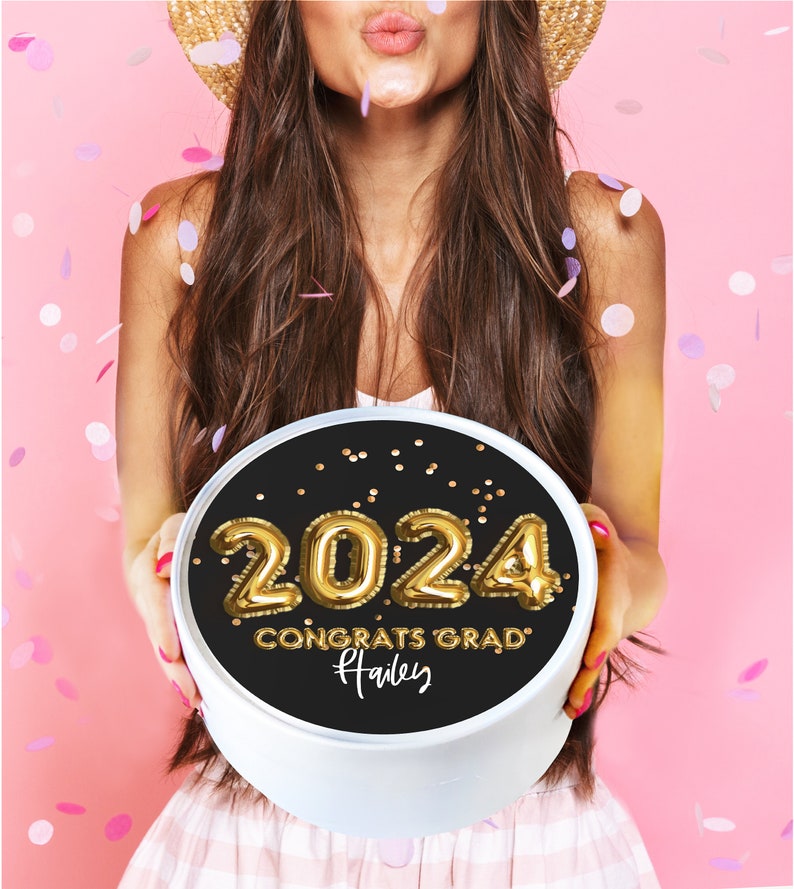 May include: A black and white round box with a gold 2024 balloon number design. The box has gold confetti and the text "Congrats Grad" with the name "Hailey" written in cursive.