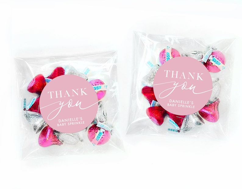 Peut inclure: Des sachets de faveur roses et argent&eacute;s remplis de baisers au chocolat et un autocollant rond rose avec du texte blanc qui dit "THANK you" et "DANIELLE'S BABY SPRINKLE".