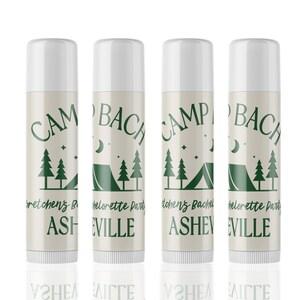 May include: Four white lip balm tubes with green text and graphics. The text reads "Camp Bachelorette Party" and "Camp Bachelor Party" with the location "Asheville" or "Eville".