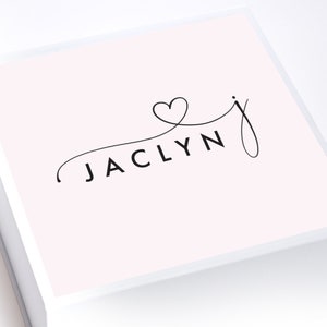May include: A white gift box with a pink lid. The lid has a black cursive font that says "JACLYN" with a heart symbol above the "J".