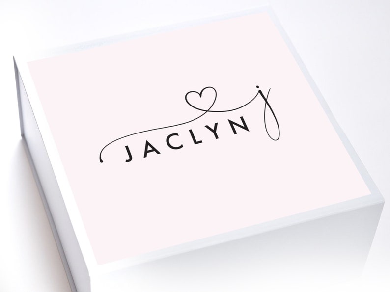 May include: A white gift box with a pink lid. The lid has a black cursive font that says "JACLYN" with a heart symbol above the "J".