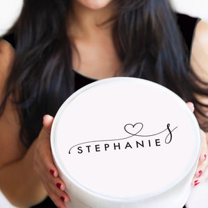 Puede incluir: Caja de regalo redonda blanca con una fuente negra cursiva que dice "STEPHANIE" con un s&iacute;mbolo de coraz&oacute;n sobre la "S".