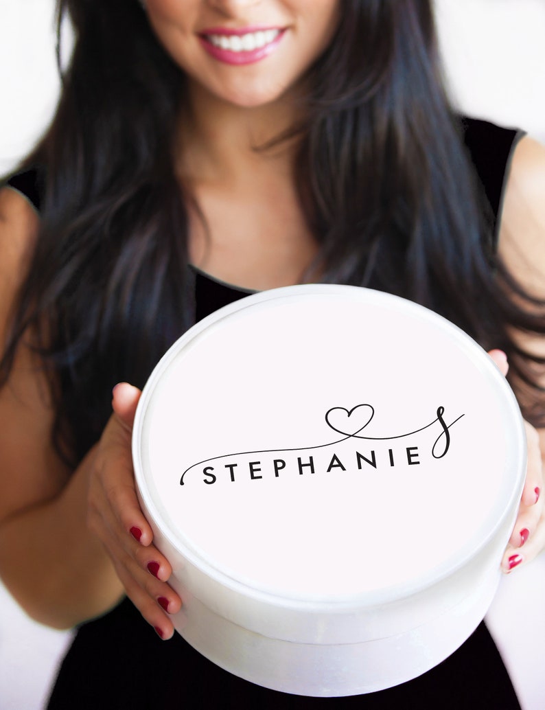 Puede incluir: Caja de regalo redonda blanca con una fuente negra cursiva que dice "STEPHANIE" con un s&iacute;mbolo de coraz&oacute;n sobre la "S".