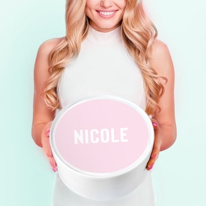 May include: A white round box with a pink lid. The lid has the name "NICOLE" printed in white letters.