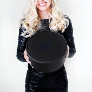 May include: A solid black circular box with a smooth matte finish and a matching lid. The container features a simple cylindrical shape with clean edges, presenting a uniform dark appearance throughout the entire exterior surface of the object.