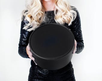 May include: A solid black circular box with a smooth matte finish and a matching lid. The container features a simple cylindrical shape with clean edges, presenting a uniform dark appearance throughout the entire exterior surface of the object.