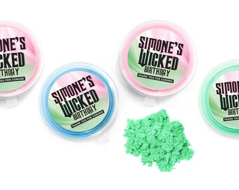 Può includere: Quattro contenitori rotondi in plastica riempiti con sabbia modellabile colorata, ognuno con un'etichetta circolare che riporta la scritta Simone's Wicked Birthday e Thank You For Coming. Un piccolo mucchio di sabbia verde è al centro.