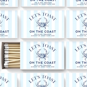 May include: A set of matchboxes with a blue and white striped design. Each box features a blue crab illustration and the text "Let's Toast On The Coast" with the wedding date and location.