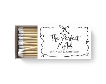 Peut inclure: Une boîte de matches blanche avec une étiquette noire et blanche qui dit "The Perfect Match" avec un nœud et le texte "MR. + MRS. JOHNSON".