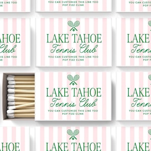 May include: A rectangular matchbox with a light pink and white vertical striped pattern. The front features a green graphic of two crossed tennis rackets and a ball, with the text LAKE TAHOE Tennis Club and YOU CAN CUSTOMIZE THIS LINE TOO POP FIZZ CLINK.
