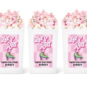 May include: Three white popcorn boxes with pink and white checkered labels. The labels have the text "Let's Roll" in pink and a retro roller skate graphic. Each box also has the text "Happy Birthday Aubrey".