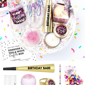 May include: A birthday gift set containing a clear stemless flute with the word yay!, a gold party horn labeled BIRTHDAY BABE, a multi-colored striped straw, a pink bath bomb, a candle in a gold tin, and a confetti popper labeled HAPPY Birthday SARAH.