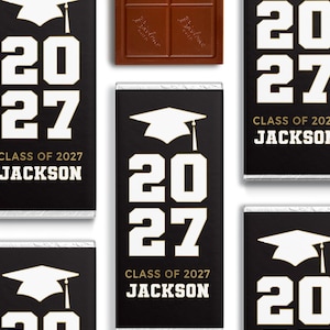May include: Chocolate bars with black wrappers featuring a graduation cap graphic, the year "2027", and the text "CLASS OF 2027 JACKSON" in white. A solid chocolate bar is also visible. The bars are arranged on a white background.