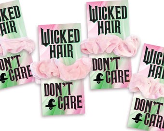 May include: Four light pink fabric hair scrunchies attached to individual rectangular display cards. Each card features a green and pink gradient background with the black text WICKED HAIR DON'T CARE and a small black witch hat icon.