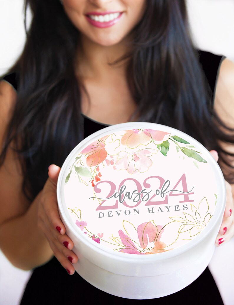 May include: White round gift box with a pink floral design and gold accents. The box has the text "Class of 2024" and "DEVON HAYES" printed on it.