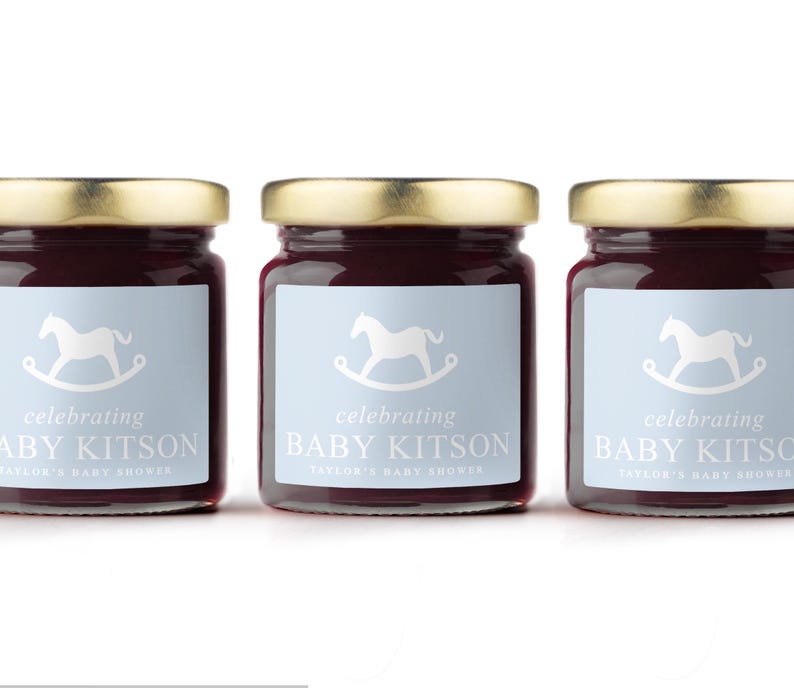 May include: Three glass jars filled with a dark red preserve, each topped with a gold lid. The jars have light blue labels with a white rocking horse and the text "celebrating BABY KITSON TAYLOR'S BABY SHOWER."