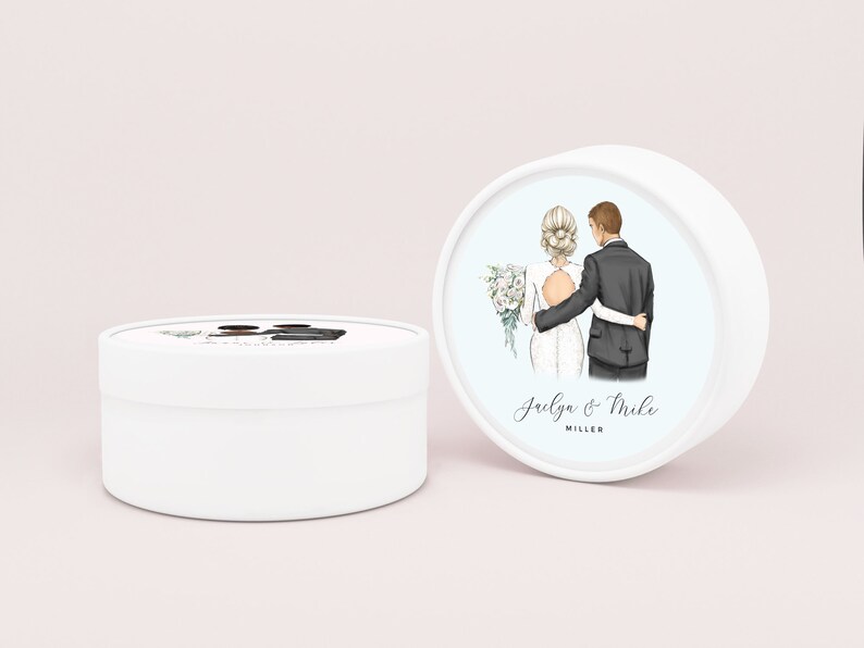 May include: White round favor box with a couple's illustration on the lid. The bride is wearing a white dress and the groom is wearing a black suit. The text on the lid reads "Jaelya & Mike MILLER".