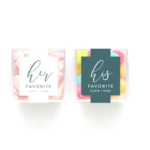 May include: Two clear plastic containers filled with colorful candies. One container has a white label with the text "her favorite cloie + zack". The other container has a teal label with the text "his favorite cloie + zack".