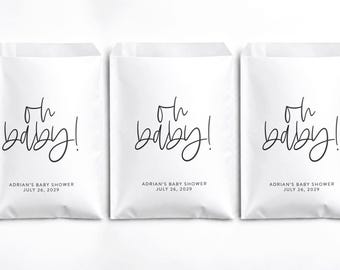 May include: Three white paper bags featuring the black text "oh baby!" in a cursive script, followed by the printed text "ADRIAN'S BABY SHOWER" and "JULY 26, 2029" in a simple sans-serif font centered on the front of each bag.