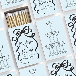 May include: Light blue matchboxes with a black and white illustration of a champagne tower and a bow. The text on the matchbox reads "Madison & David" with the date "June 18, 2025" and the location "Napa Valley".