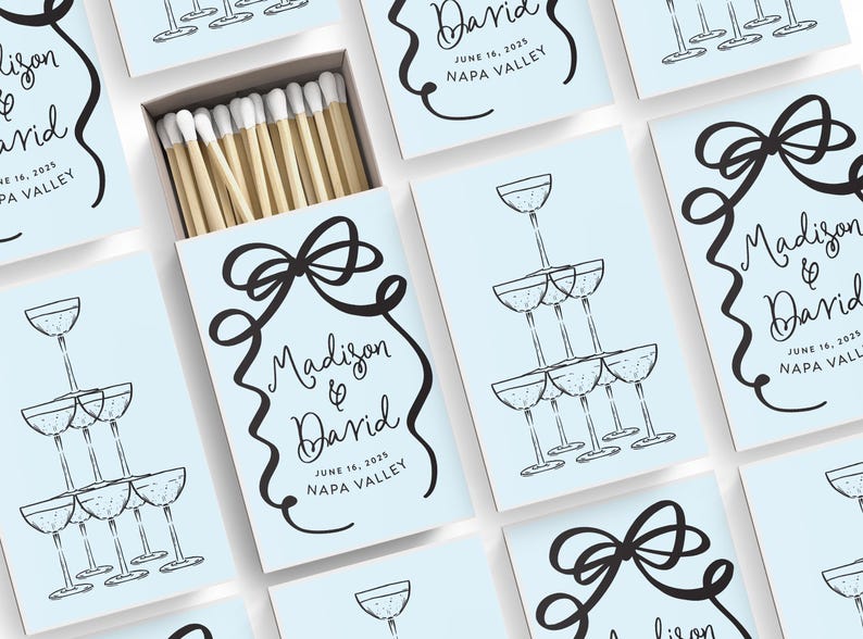 May include: Light blue matchboxes with a black and white illustration of a champagne tower and a bow. The text on the matchbox reads "Madison & David" with the date "June 18, 2025" and the location "Napa Valley".
