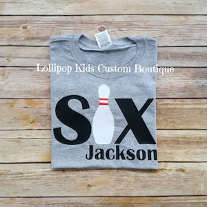 May include: Gray t-shirt with black text that says "Six" with a white bowling pin in the middle of the word. The text "Jackson" is below the word "Six".