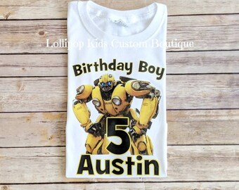 May include: White t-shirt with a yellow Bumblebee Transformer character, the number 5, and the name Austin printed in black. The text "Birthday Boy" is printed above the character.