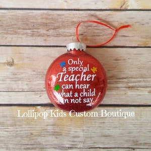 May include: Red glitter Christmas ornament with the text "Only a special Teacher can hear what a child can not say."