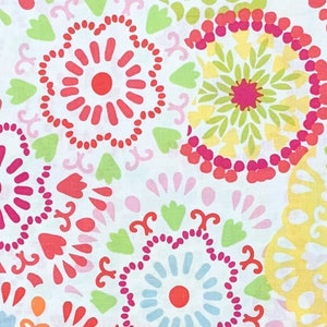 May include: A close-up of a white fabric with a repeating pattern of colorful floral designs. The pattern includes circular shapes in shades of red, pink, yellow, green, and blue. The floral elements are set against a white background.