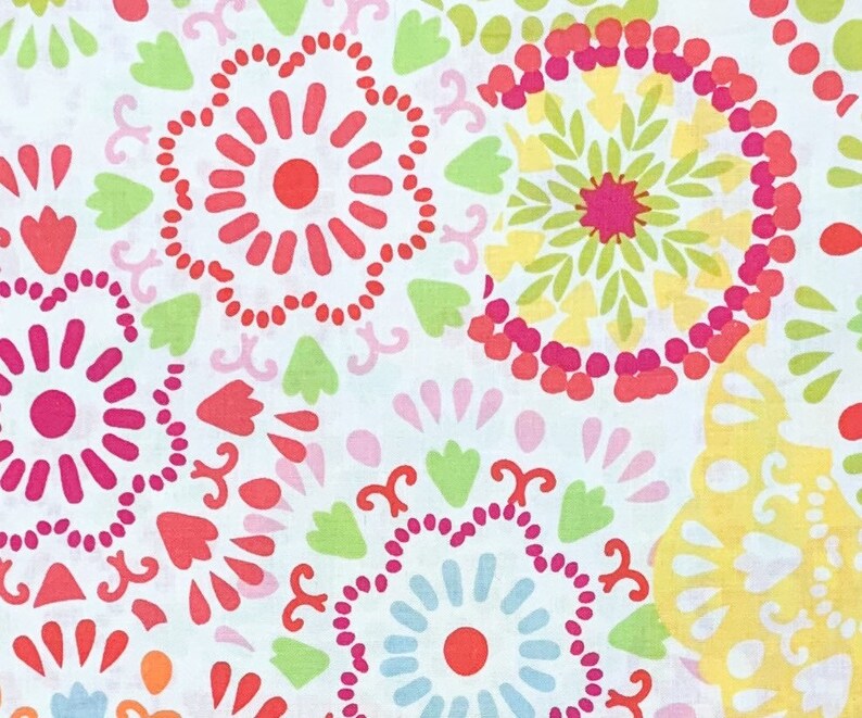 May include: A close-up of a white fabric with a repeating pattern of colorful floral designs. The pattern includes circular shapes in shades of red, pink, yellow, green, and blue. The floral elements are set against a white background.